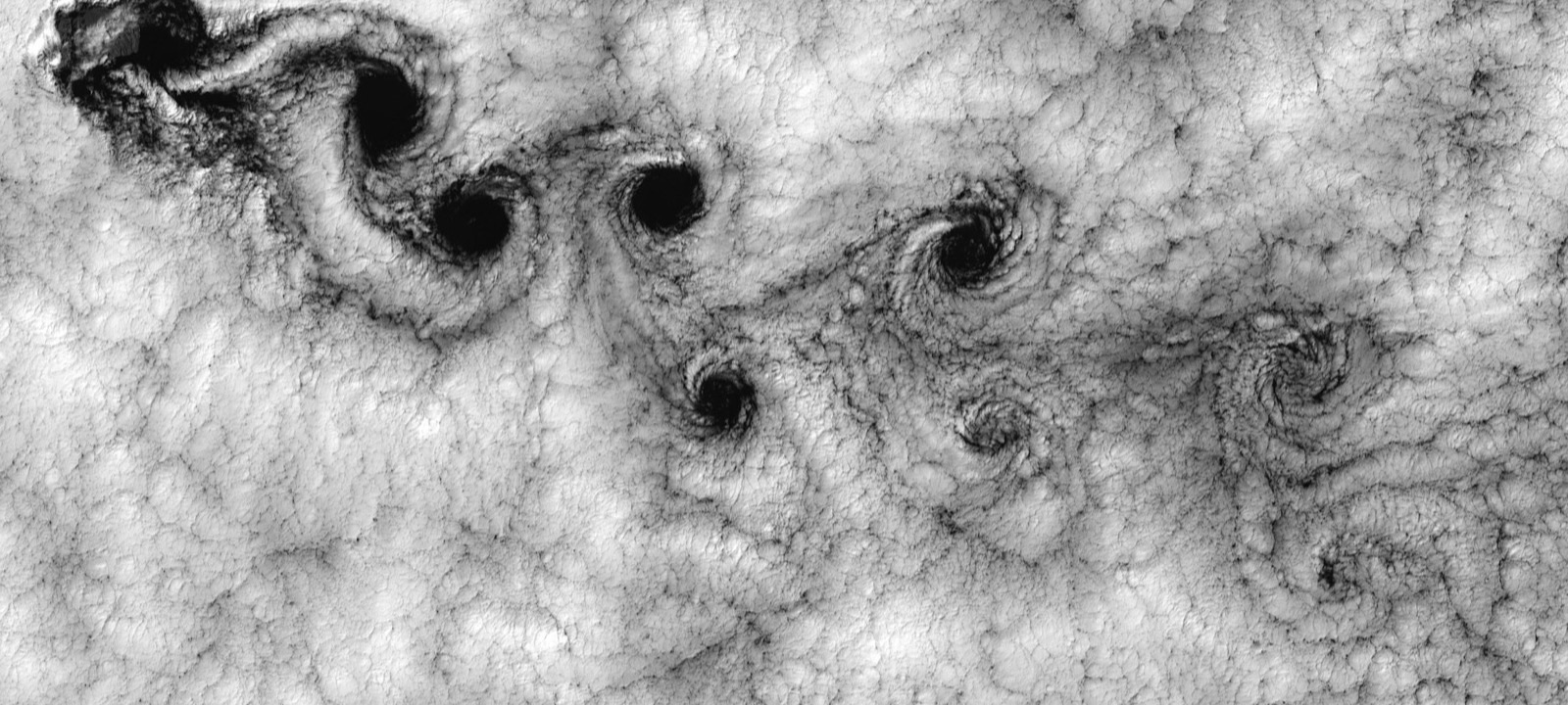 Clouds streaming past an island, forming a trail of vortices that turn in alternate directions.